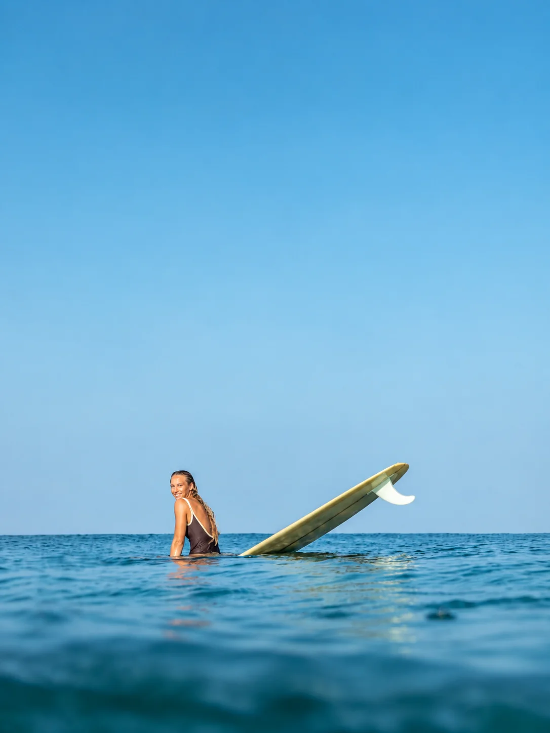 A surfer sitting in the water beside her longboard off Imi Ouaddar