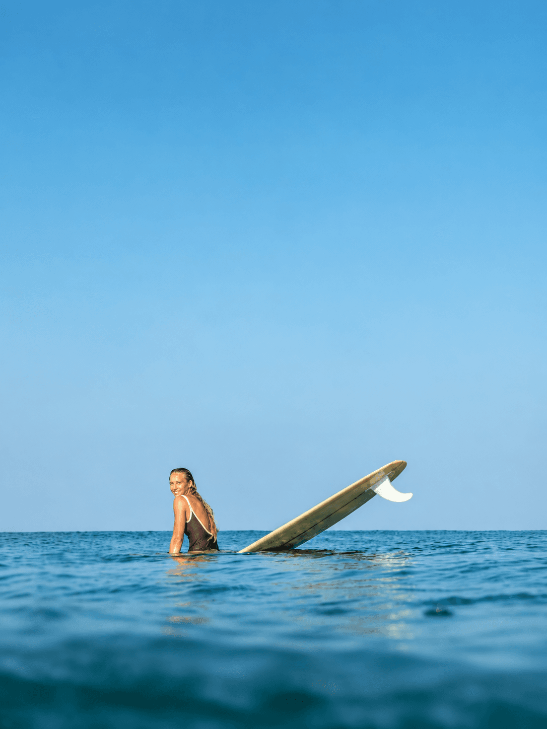 A surfer sitting in the water beside her longboard off Imi Ouaddar